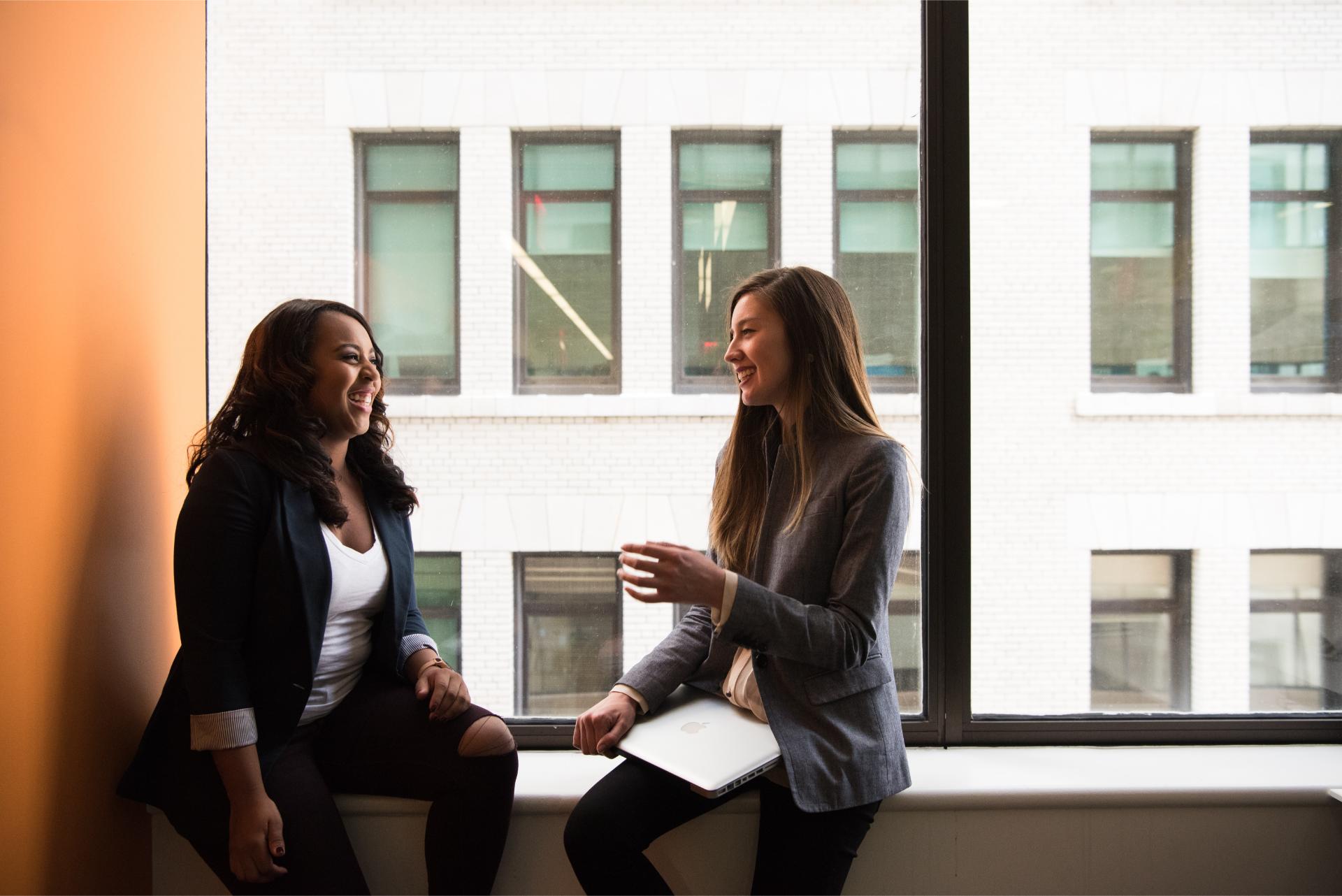 Two women chatting, sitting by window