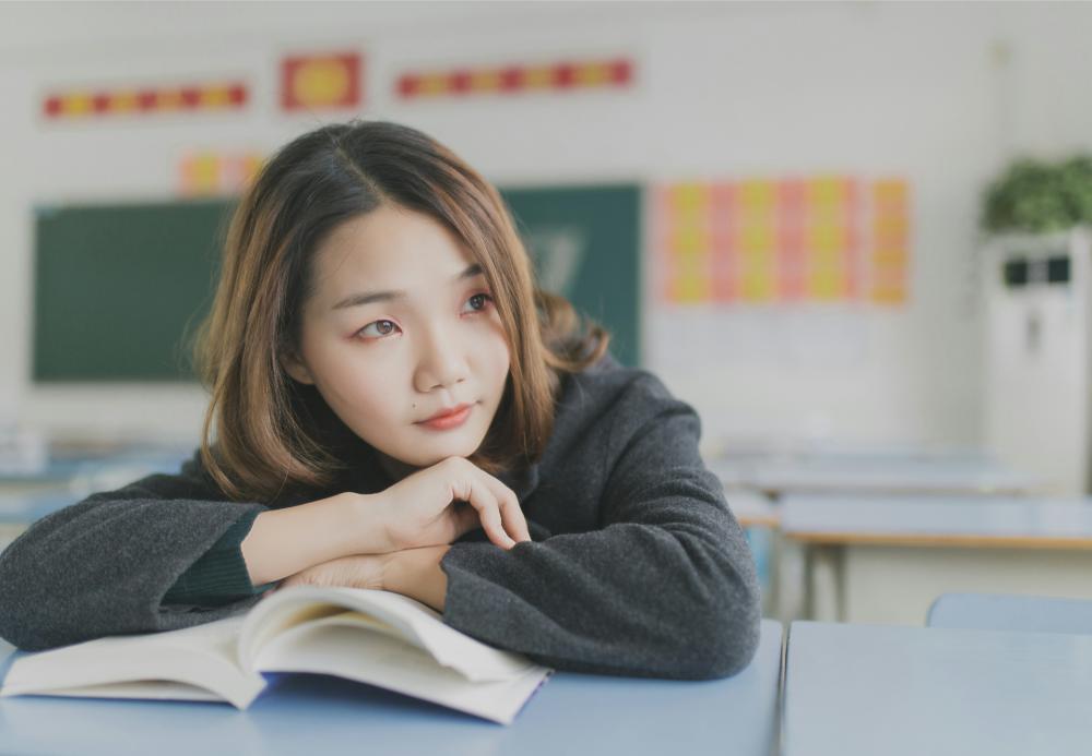 Thoughtful woman with book in classroom
